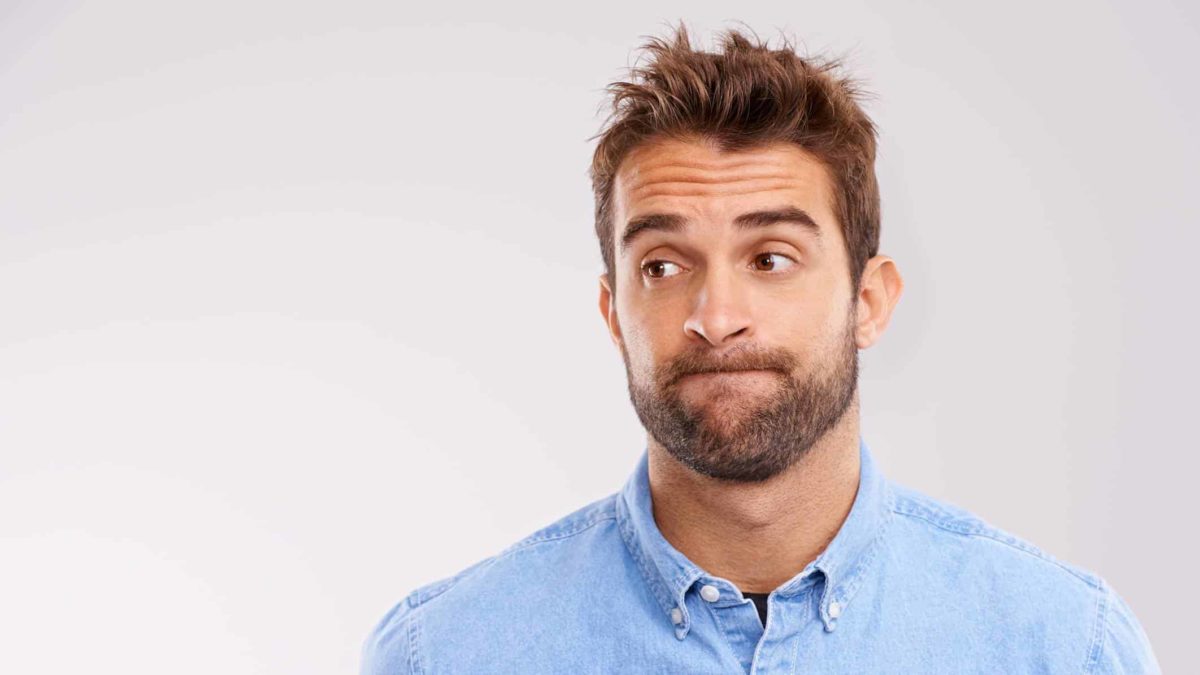 A male investor wearing a blue shirt looks off to the side with a miffed look on his face as the share price declines.