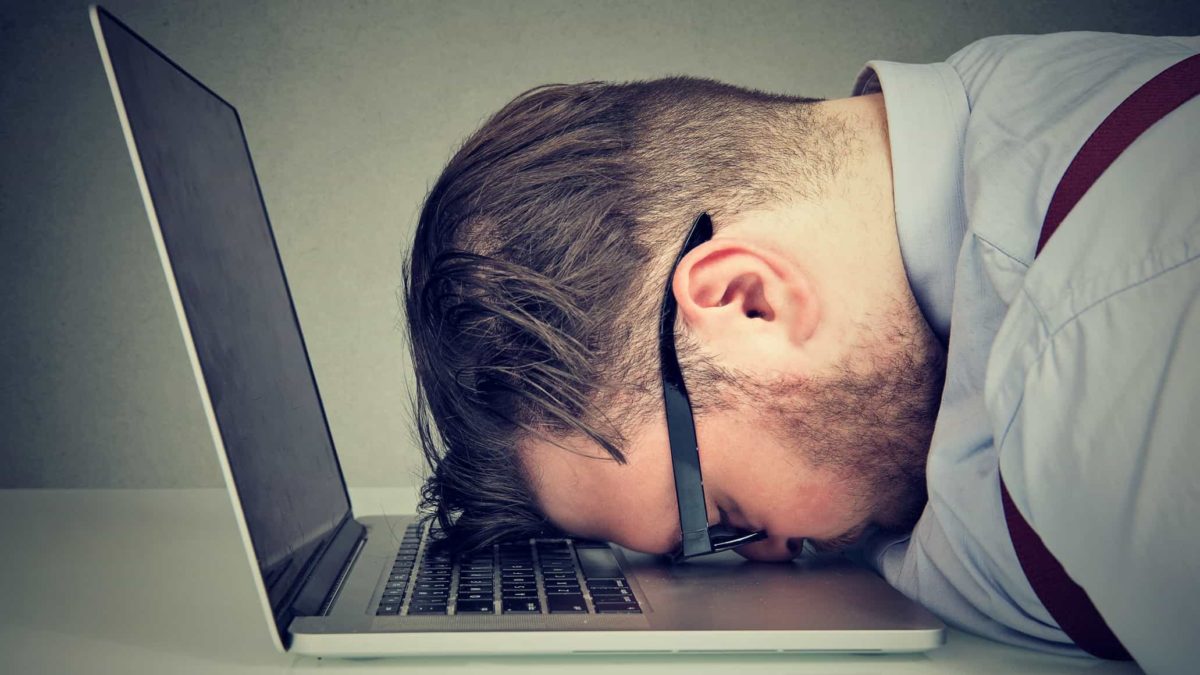 A close up picture taken from the side of a man with his head face down on his laptop computer keyboard as though he is in great despair over a mistake or error he has made or bad news he has received.