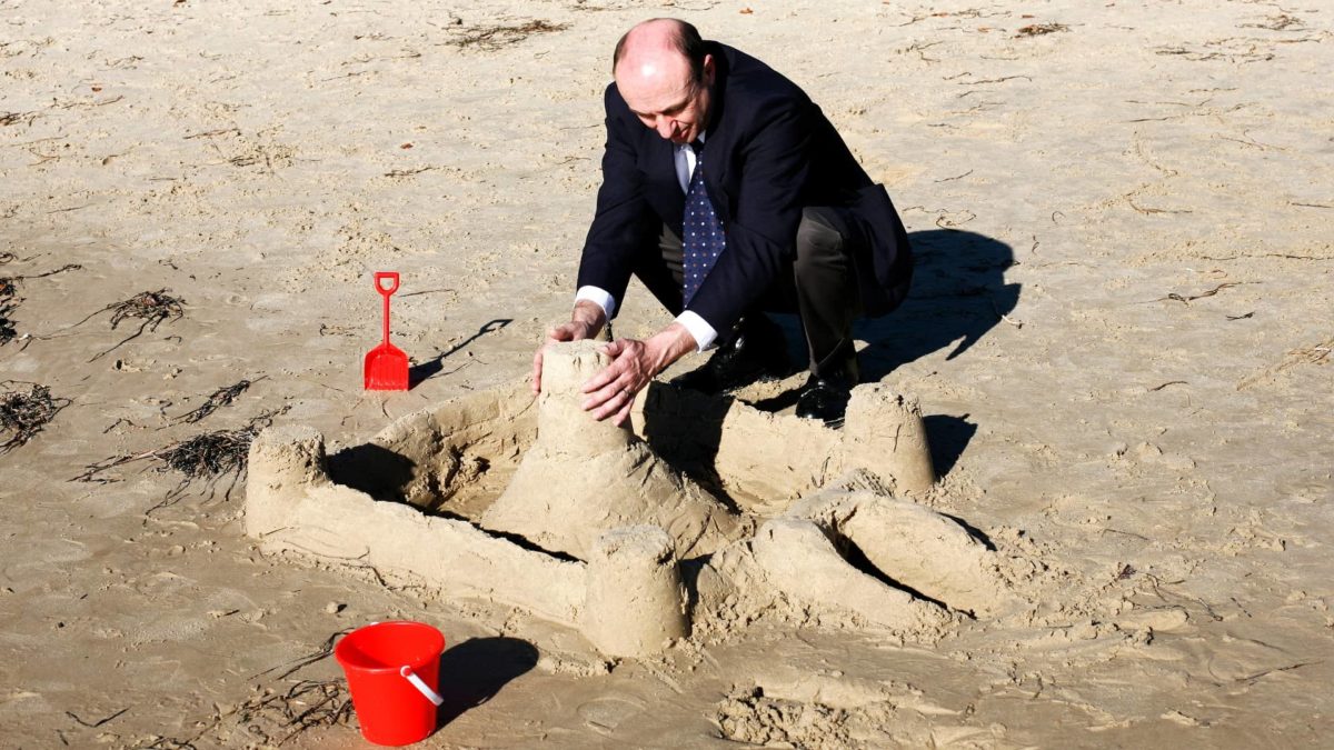 Businessman at the beach building a wall around his sandcastle, signifying protecting his business.