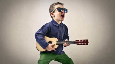 A young kid with dark glasses rocks out with a guitar.