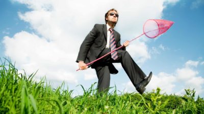 A businessman holding a butterfly net looks around hoping to snare a good ASX share investment