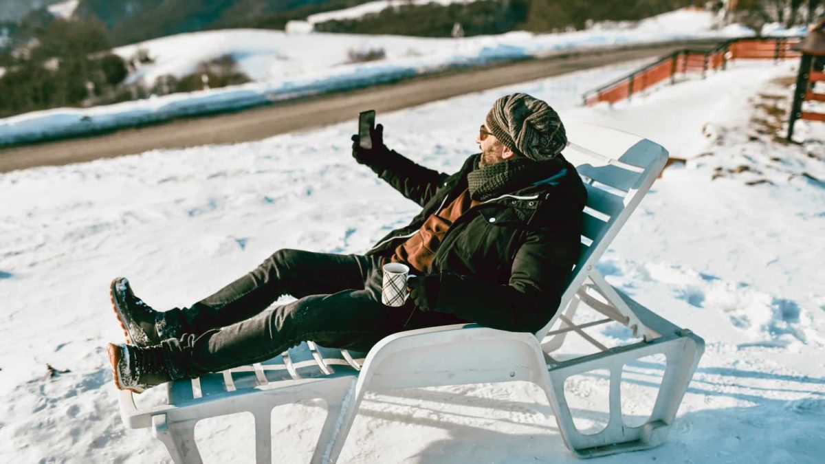 A punter sitting in the snow on a deck chair places bets on his mobile phone.
