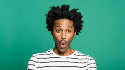 A young man wearing a black and white striped t-shirt looks surprised.