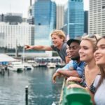 A group of young people lean over the rails overlooking Sydney's Circular Quay and check out the sights of the city around them.