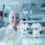A woman researcher holds a finger up in happiness as if making the 'number one' sign with a graphic of technological data and an orb emanating from her finger while fellow researchers work in the background.