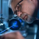 A technical manufacturer checks his work in a high-tech lab with precision equipment in the background.