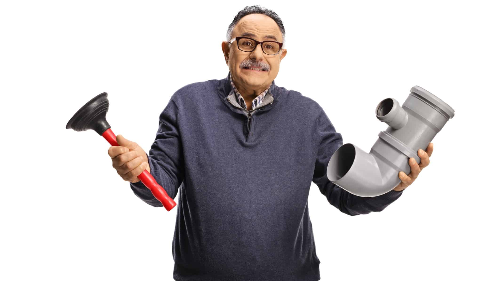 A middle aged man with a moustache and wearing casual clothes holds a plumbing plunger in one hand a a piece of toilet pipe in the other with an exasperated look on his face.