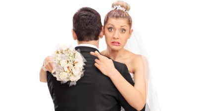 A bride looks over the shoulder of her groom with a grimace on her face.