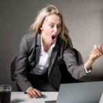 A businesswoman gets angry, shaking her fist at her computer.