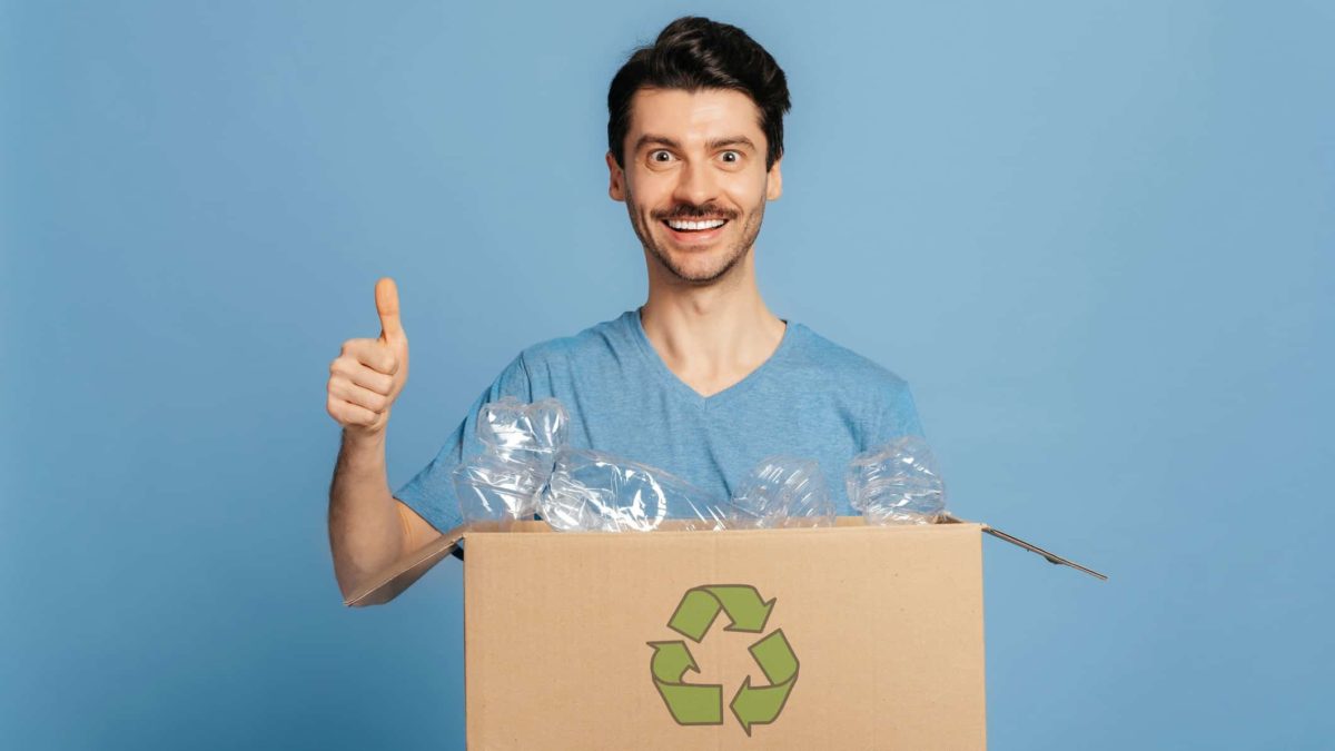 A man holding a packaging box with a recycle symbol on it gives the thumbs up.