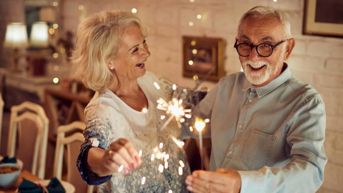 An older couple come together in their warm heated home with fire cracker sparklers.