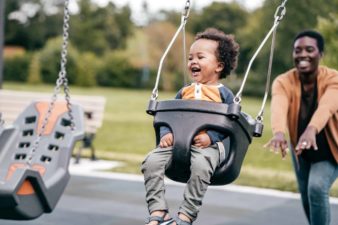 Smiling adult pushing toddler on a swing at the park.