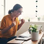 A woman is very excited about something she's just seen on her computer, clenching her fists and smiling broadly.