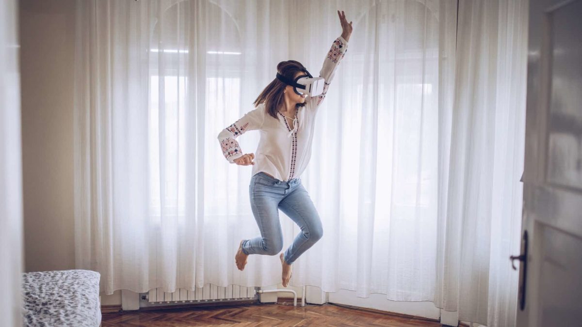A woman wearing a virtual reality headset jumps high in her living room.