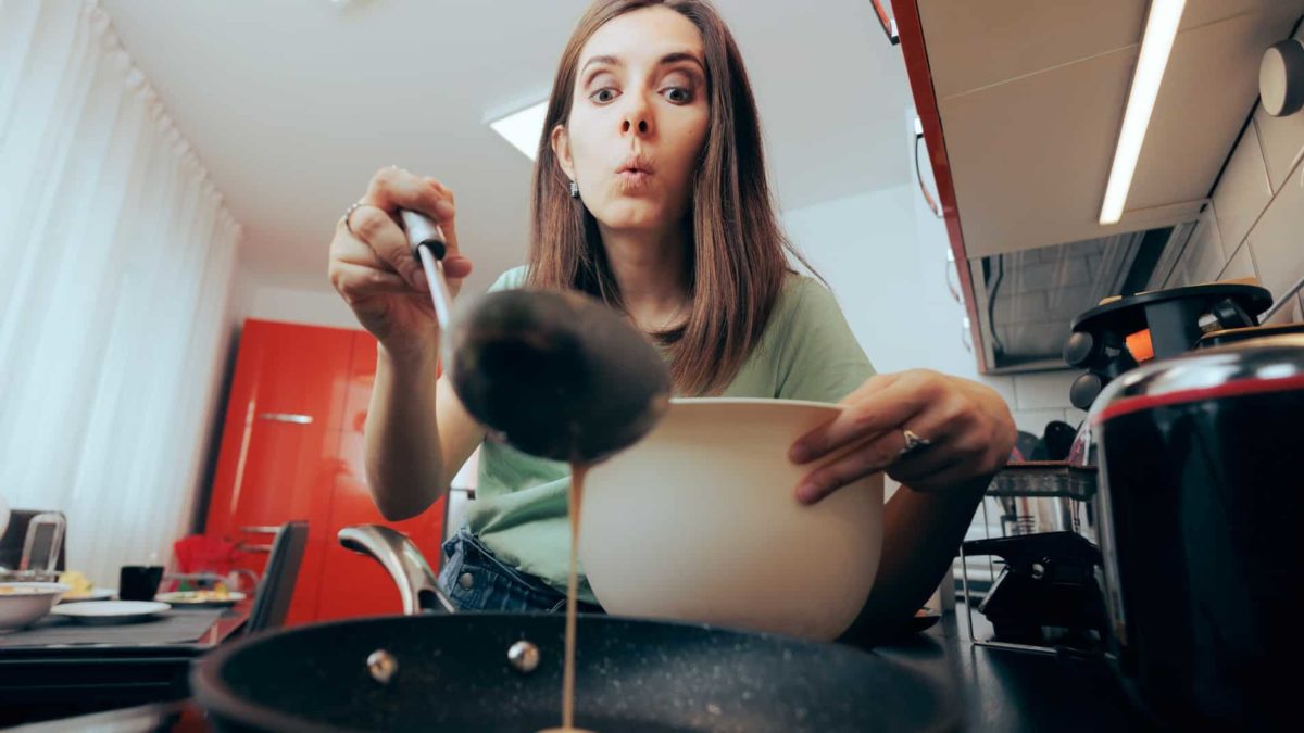 A woman looks unsure as she ladles mixture into a pan surrounded by small appliances