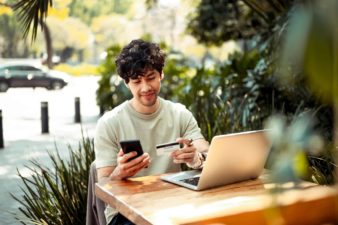 person sitting at outdoor table looking at mobile phone and credit card.