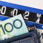 A wallet with a one hundred dollar bill poking out sits on top of an electricity meter with the numbers rapidly going up, representing power prices in Australia rising as we ponder whether the Origin Energy share price will go up as a result