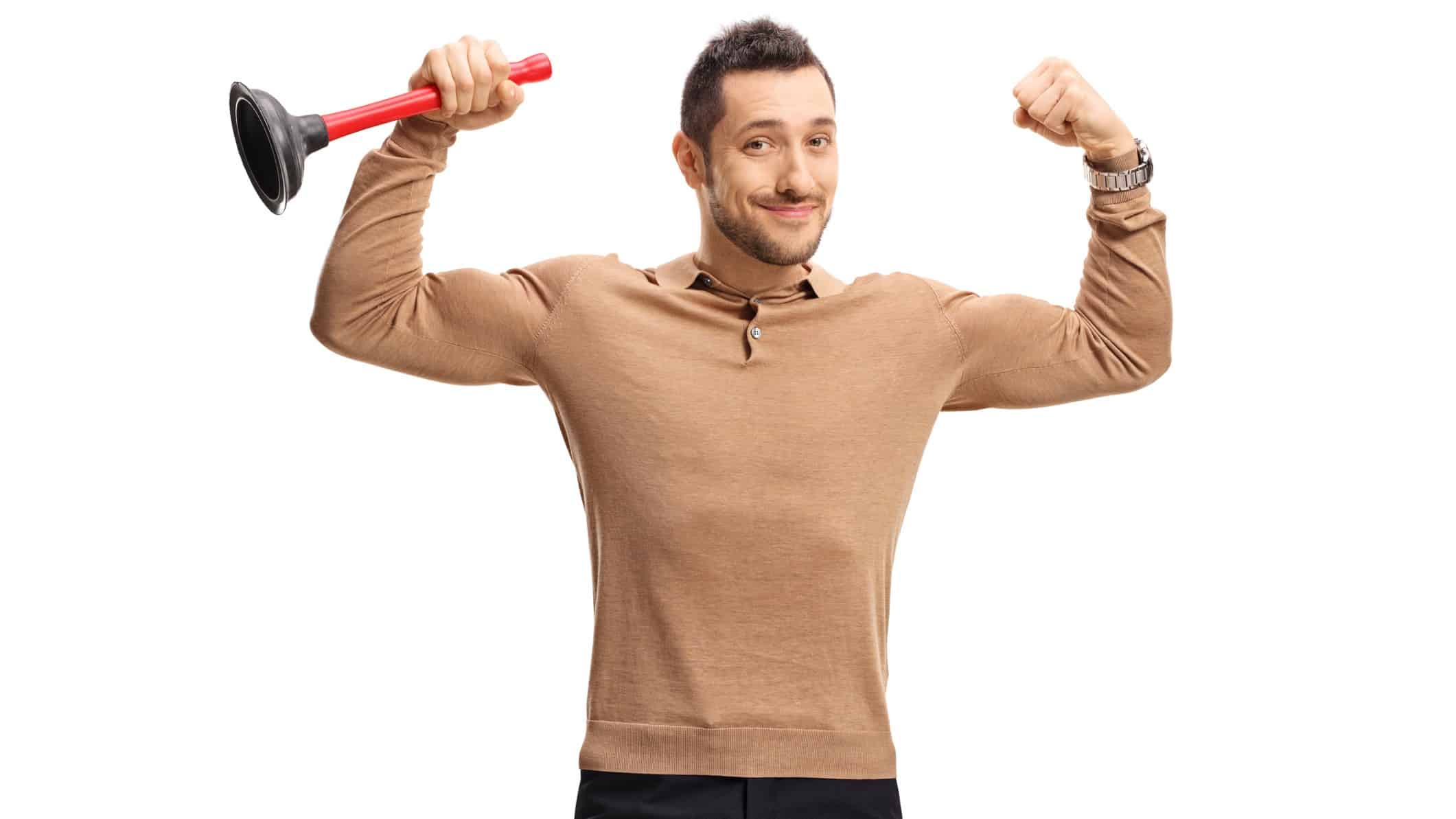 a man holds a plunger while also holding his arms aloft in a pose to show off his muscles and strength with a wry smile on his face.