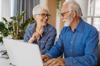 A couple working on a laptop laugh as they discuss their ASX share portfolio.