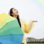 A happy woman holding an umbrella in front of a rainbow.