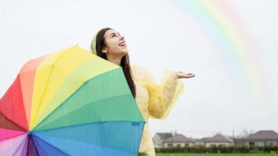 A happy woman holding an umbrella in front of a rainbow.