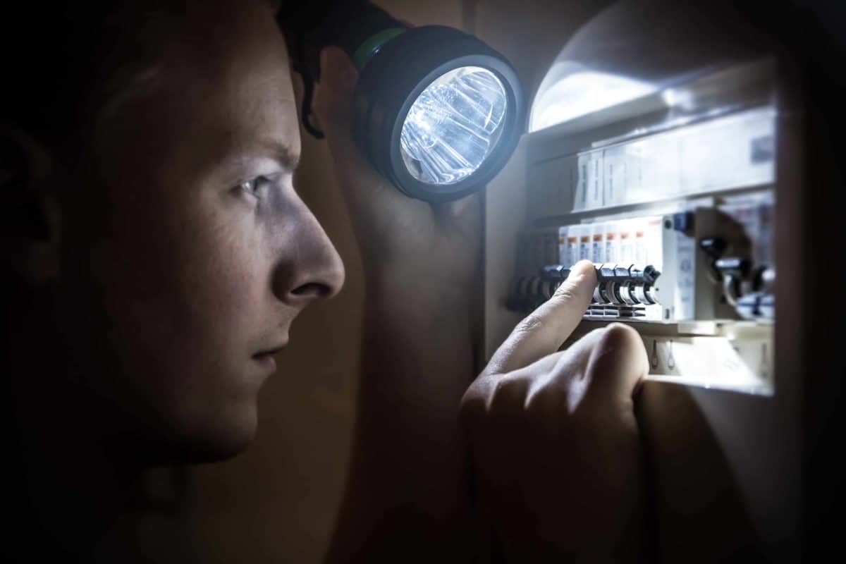 An electrician looks at a power board using a torch in the dark