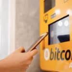 A person's hand is seen operating a Bitcoin ATM