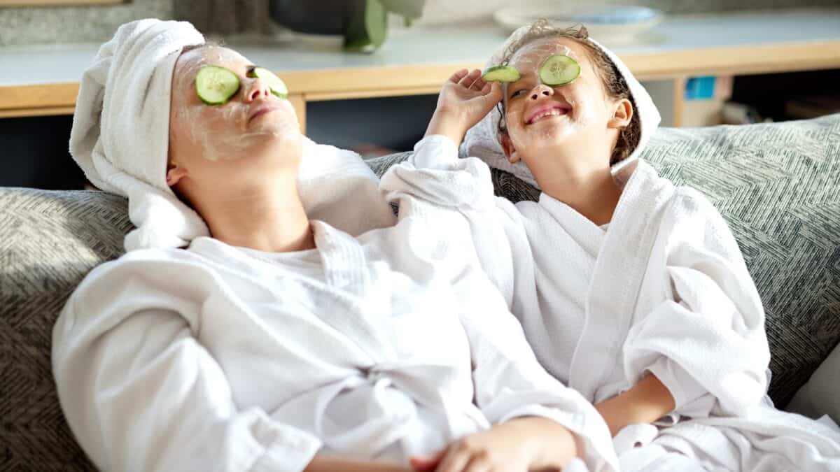 A happy woman and girl kick back on a couch in spa robes with cucumbers on their eyes, indicating they can earn passive income while relaxing.