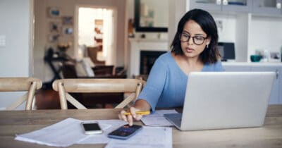 A young woman uses a laptop and calculator while working from home.