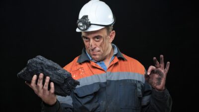 Coal miner holding a giant coal rock in his hand making a circle with his hand, symbolising a rising share price.