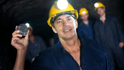 Group of miners working at a coal mine with one smiling and holding up a piece of coal.