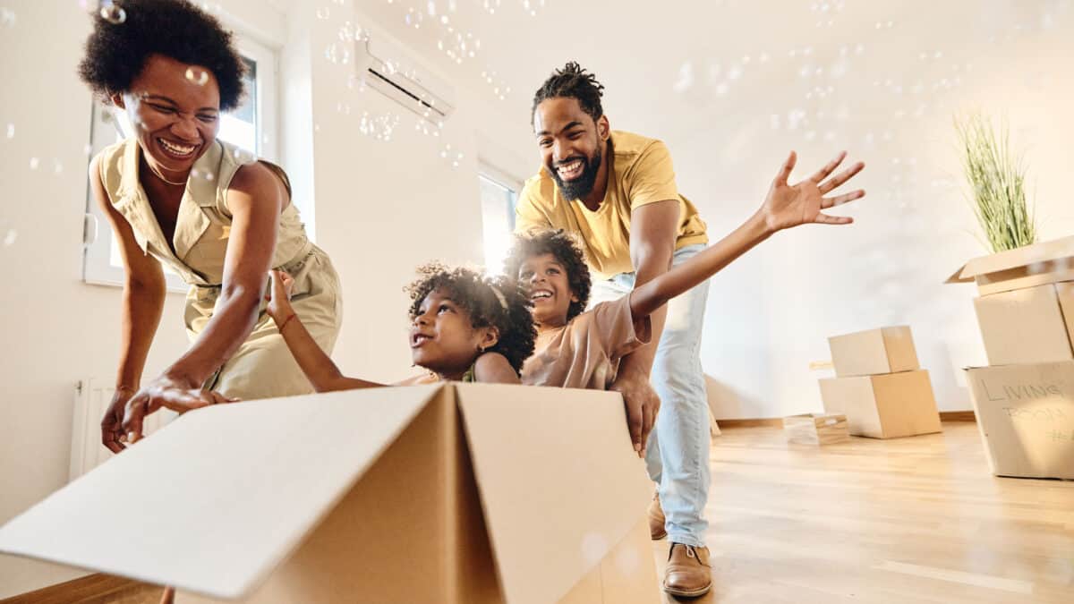 Playful parents having fun while pushing their small kids in cardboard box as they move into their new home.