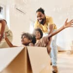 Playful parents having fun while pushing their small kids in cardboard box as they move into their new home.