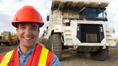 Miner standing in front of trucks and smiling, symbolising a rising share price.