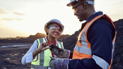 Two young African mine workers wearing protective wear are discussing coal quality while on site at a coal mine.