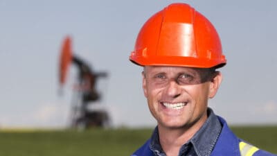 Smiling oil worker in front of a pumpjack.