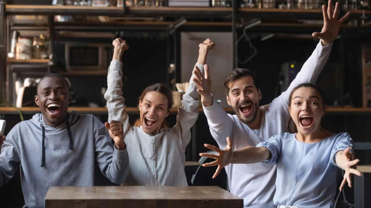 Multi-ethnic people looking at camera sitting at public place screaming, shouting and feeling overjoyed about their windfall, good news or sports victory.