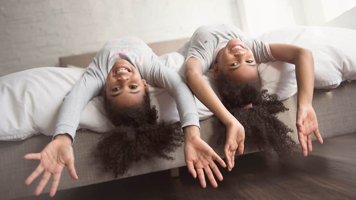 The Two little girls smiling upside down on a bed.