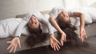 The Two little girls smiling upside down on a bed.
