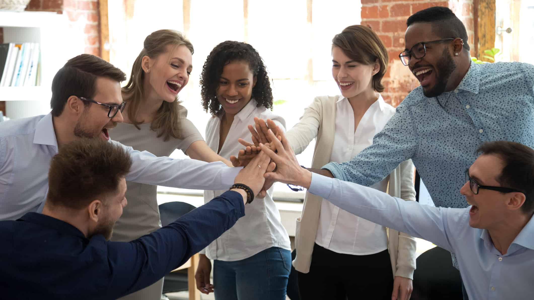A diverse group of happy office workers join hands in a team high five in celebration of a job well done.