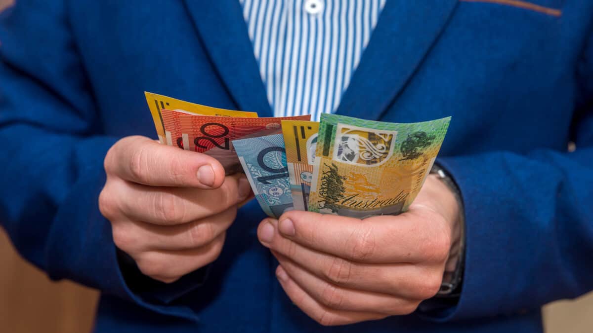Male hands holding Australian dollar banknotes, symbolising dividends.