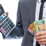 Man holding a calculator with Australian dollar notes, symbolising dividends.