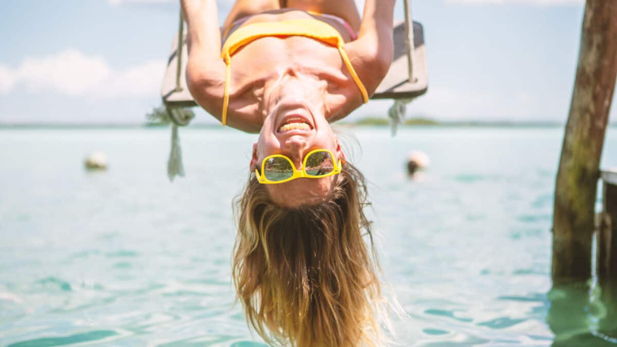 Smiling woman upside down on a swing with yellow glasses, symbolising passive income.