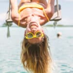 Smiling woman upside down on a swing with yellow glasses, symbolising passive income.