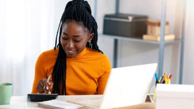 Close up of woman using calculator and laptop for calculating dividends.