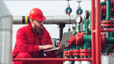 Worker on a laptop at an oil and gas pipeline.