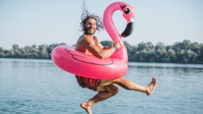 Man jumping in water with a floatable flamingo, symbolising passive income.