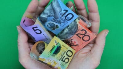 Different Australian dollar notes in the palm of two hands, symbolising dividends.