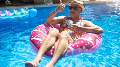 A retiree relaxing in the pool and giving a thumbs up.