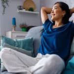 Woman smiling with her hands behind her back on her couch, symbolising passive income.